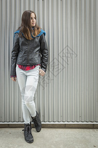 年轻女孩穿着皮夹克站在金属墙边望着另一图片