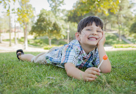 英俊的年轻男孩喜欢他的棒糖户外在草地上图片