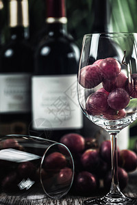 装满红葡萄的酒杯各种红葡萄酒瓶子木碗里的坚果和背景新鲜葡萄图片