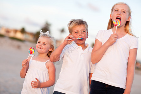 吃棒棒糖可爱的兄弟和姐妹们享受他的棒糖在海滩上背景