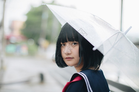 城市的亚洲女学生看着雨伞图片