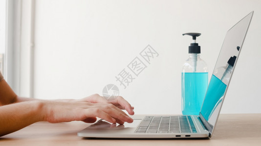 在笔记本电脑上工作之前使用酒精凝胶清洁剂洗手以保护冠状女在家中和自我隔离时在社会不和将酒精推向清洁卫生图片