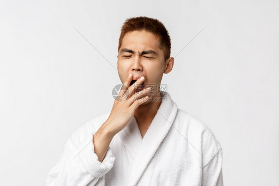 美spa和休闲概念年轻亚洲人困睡男子的肖像闭着眼睛打哈和遮盖嘴部戴浴袍在度假白色背景期间在旅馆醒来白色背景中醒来美spa和休闲概图片