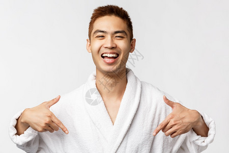 美丽娱乐和休闲概念满意快乐和的浴袍中亚洲男子肖像指着自己笑得广泛谈论自己的成就个人功白色背景美丽快乐和的浴袍中亚洲男子肖像谈论自图片