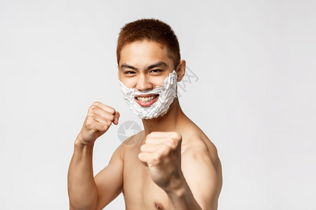美丽人与卫生概念英俊的亚洲男子在浴室镜附近玩耍做出自信的表情站在拳击姿势上刮胡子在脸上涂剃须霜英俊的亚洲男子在浴室镜周围玩弄表现图片