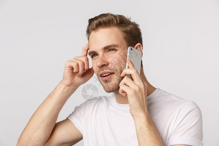 深思熟虑的金发年轻男子在电话上讲抓着头部通过手机思考什么顺序握着智能手机靠近耳朵斜视思考答案白色背景深思不自信的金发年轻男子在电图片
