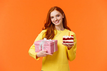 可爱的红发女孩带着包装的礼物和美味白日蛋糕来参加派对问朋友吹风蜡烛和庆祝女朋友生日微笑在橙色背景上可爱的红发女孩带着包装的礼物和图片