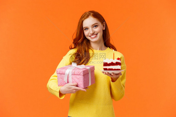 可爱的红发女孩带着包装的礼物和美味白日蛋糕来参加派对问朋友吹风蜡烛和庆祝女朋友生日微笑在橙色背景上可爱的红发女孩带着包装的礼物和图片
