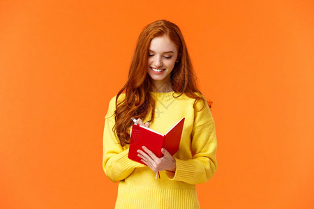 20岁写在她的日记填入待办清单或个人时间表新的笔记本微笑着一切有计划站着橙色背景无忧腰上吸引着红发女孩写在她的日记填入待办清单或图片