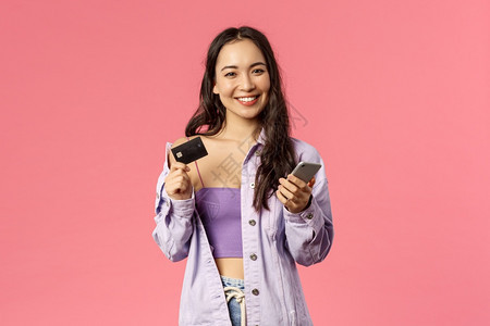 年轻时装女孩的肖像微笑快乐的相机使用手和持有信卡支付网上购买互联商店订购食品站立粉红色背景的信用卡年轻时装女孩的肖像微笑高兴的相图片