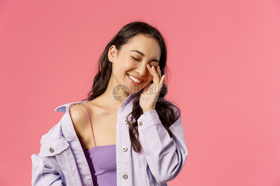 有趣的对话粉红色背景生活方式人与情感概念喜悦有时髦的韩国女孩笑抚摸眼睛闭着微笑有趣的对话摸着眼睛闭笑有趣的交谈图片