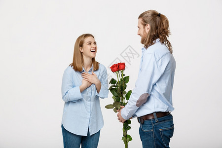英俊优雅男子的肖像令人惊讶他美丽的女友带着红玫瑰却在白色孤立的背景下笑着英俊优雅男子的肖像则令人惊讶图片