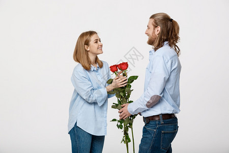 英俊优雅男子的肖像令人惊讶他美丽的女友带着红玫瑰却在白色孤立的背景下笑着英俊优雅男子的肖像则令人惊讶图片