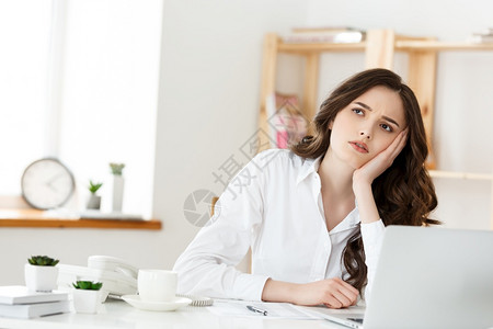 深思熟虑的女士坐在笔记本上电脑旁边眼神不振办公室员工感到缺乏灵动力图片