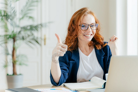 红头发的妇女一直举起拇指表现出像手势一样对同事的出色工作感到满意更新现代工具软件在网站上搜索数据在工作空间中展示图片