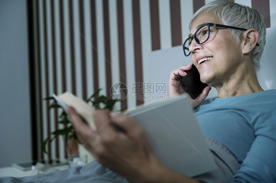 睡在卧室中床上的成年妇女患有失眠症躺在床上通过电话交谈和阅读一本书睡在觉中不的成年妇女患有失眠症通过电话交谈和在床上阅读一本书图片