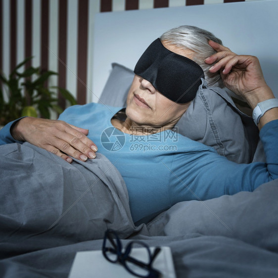 身戴黑睡面具躺在卧室床上的成年妇女身戴黑睡面具躺在床上的成年妇女图片