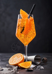 一杯有橙色片的aperolsitz夏季鸡尾酒和黑色底有冰块的吉格机图片