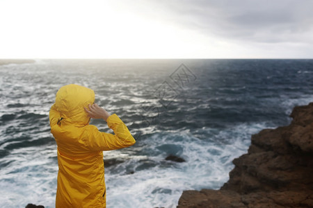 穿黄色雨衣的女子站在悬崖上仰望大海图片