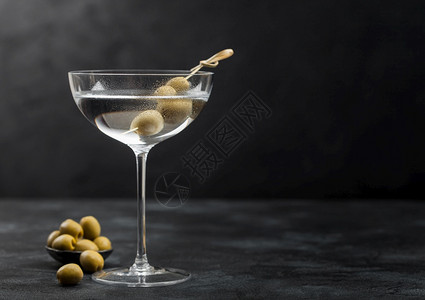 伏特加马提尼酒鸡尾在现代玻璃杯里橄榄在金属碗里竹棍在黑色背景上图片