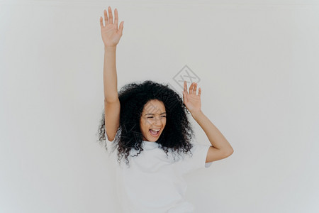 欢喜的卷非洲女举起手来欢笑幸福喜成功穿白T衬衫室内装饰积极姿势出乎意料的惊喜图片