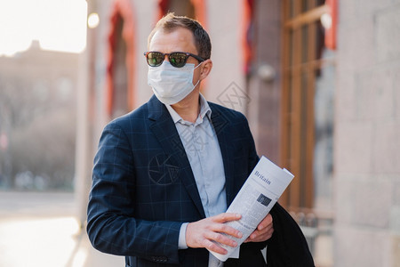 商人戴防传染病的保护面罩阅读报纸穿着优雅在户外布置思考如何防止的新冠状图片