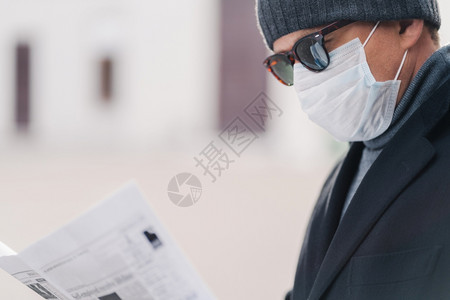 男模型的作物片防止传染疾病或冠状毒戴卫生面具以防止感染呼吸道疾病阅读报纸在隔离城市户外传播图片