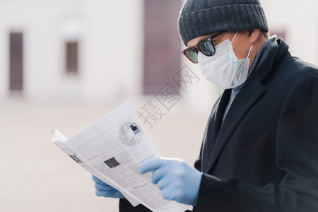 成年男子横向拍摄戴保护面罩和一次手套阅读新鲜报纸了解有关流行病情况的消息图片