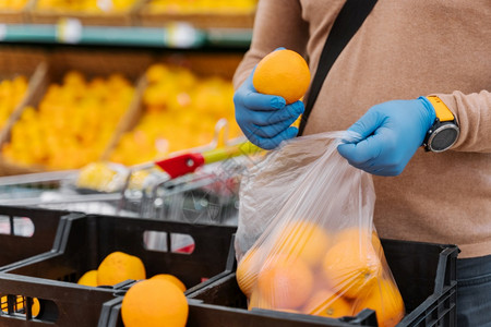 无脸男子买家在购物中心选择新鲜橙子害怕冠状在爆发时戴橡胶手套购买产品或食图片