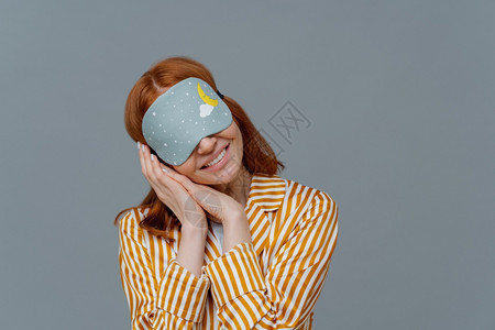 微笑的温柔女士戴面罩倾斜头棕榈穿条纹睡衣涂在灰墙上复制文本的空间感觉舒适放松图片