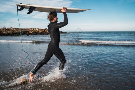 年轻冲浪者穿着黑色服带着板进入水中运动和的概念图片