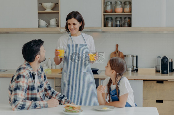 母亲穿着围裙端着两杯果汁给丈夫和女儿图片