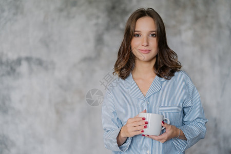 穿夜衣的有吸引力女子用咖啡或茶白色杯子或咖啡茶用白色杯子喝早酒以模糊的背景在室内装饰并有供广告或宣传内容的复制空间背景图片