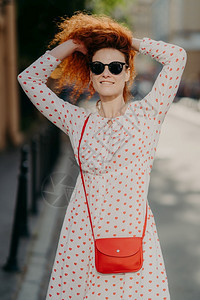 快乐的美丽女人红发戴头巾太阳眼镜穿白裙子带红包享受阳光明媚的一天流浪街头人生活方式暑假概念图片