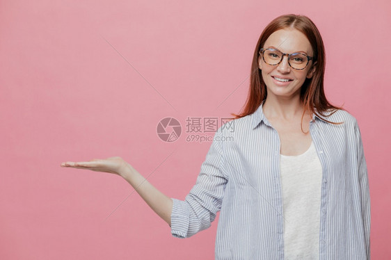 令人愉快的causin女人工作室拍摄快乐的causin女人保持棕榈戴光眼镜展示一些东西超越复制空间保持白脸上笑容愉快室内穿过粉红图片