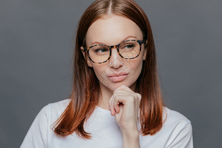 深思熟虑的causin女人满嘴胡言深褐色头发看着深思熟虑穿白衣服深思熟虑试图做出决定将面部表情放在灰墙上图片