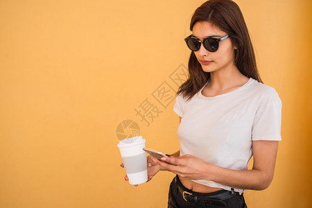 年轻女使用手机在街上举行咖啡会时使用手机的肖像图片