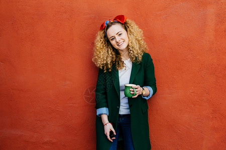 穿着头巾和时髦外套的卷发年轻时髦天主教女盛着装的绿色咖啡图片