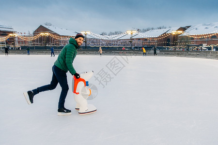 男人的横向会穿戴尖牙温暖的帽子和溜冰鞋学会滑使用辅助工具享受自由时间和冬季假期在照相机上笑图片