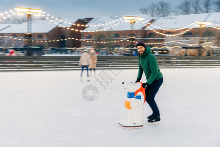 长胡子的男在户外玩新鲜空气享受寒冷的冬季天气在冰环上滑用Skae帮助害怕摔倒英俊的男人在滑冰环上玩得很开心图片