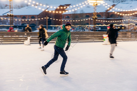 喜悦的胡须男子在冰环上滑有快乐的表情笑快乐的以他专业精神为恶魔身穿绿色夹克的活跃运动男子去参加冬季运动图片