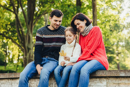 可爱的小黑板坐在户外父母之间手握叶子一起度过周末友好的年轻家庭享受在一起有快乐的表达方式坐在桥上图片