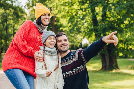 快乐的家庭在绿色公园散步快乐的表达方式亲切的父用前指向远方试图显示美丽的日落图片