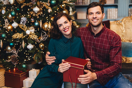 快乐的情侣坐在圣诞树旁拿着圣诞礼物图片
