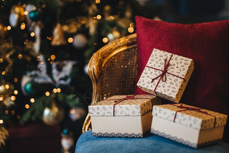 包着礼品盒的图片放在椅子上与装饰新年树背景的相配假期准备美丽圣诞树带花冠的圣诞树和室内的礼物图片