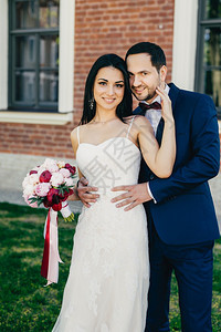 穿着白色婚纱的年轻美眉站在她英俊的新郎旁边花束上穿着正式的西装站在户外图片