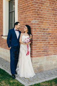 幸福的新婚夫妇站在砖墙边新娘拿着一束鲜花看她的爱人图片
