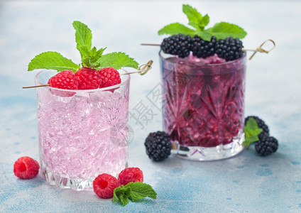 一杯黑莓清新夏季鸡尾酒和粉红色柠檬水配有冰块和薄荷放在浅蓝色背景上苏打汽水和酒精混合图片