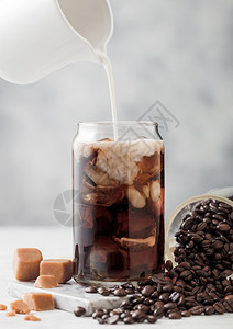 将牛奶倒入玻璃加冰黑咖啡玻璃罐豆和浅桌底盐焦糖图片