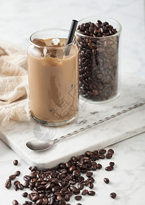 冰冷焦糖咖啡牛奶和玻璃容器豆子和勺在马贝尔板上和浅色桌底背景图片